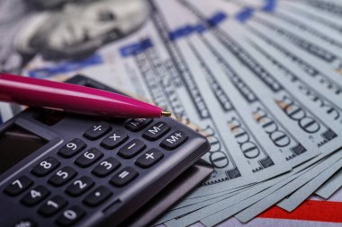 Hesap makinesinin üzerinde duran dolarlar üzerine kurulu bir kalem, yakın plan. Başarılı finansal iş kavramı. Yan üst görünüm