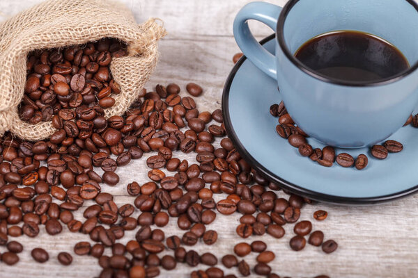 Hot, freshly brewed coffee in a blue cup and coffee beans on a light wooden table. The concept of the morning tradition of drinking coffee. Upper side view