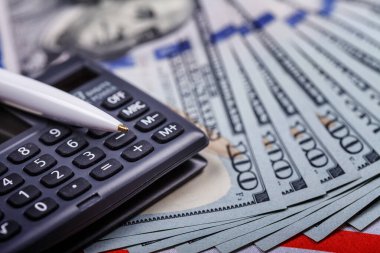 Hesap makinesinin üzerinde duran dolarlar üzerine kurulu bir kalem, yakın plan. Başarılı finansal iş kavramı. Yan üst görünüm