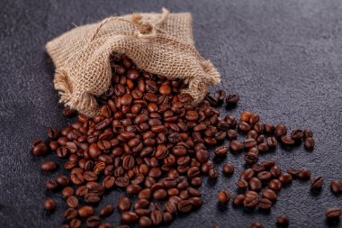 Kavrulmuş, aromatik kahve çekirdekleri, koyu bir yüzeydeki tuval torbasından serpiştirilmiş. Sabah kahvesi geleneği. Yan üst görünüm