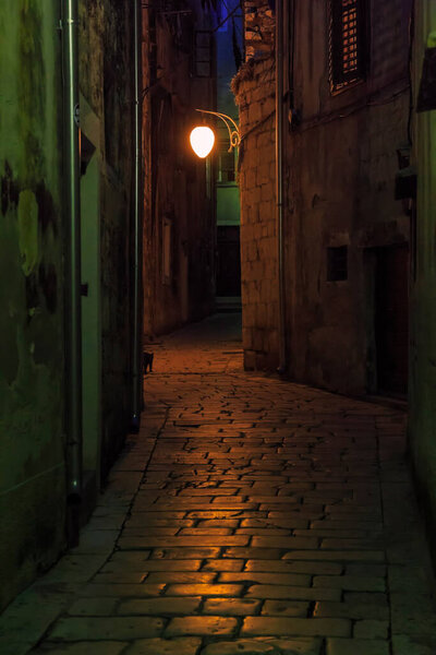 SIBENIK, CROATIA - SEPTEMBER 12, 2016: This is one of the old cobbled alleys of the seaside Croatian town lit by a red night light.