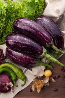 Kahverengi ahşap yüzey üzerinde kahverengi peçeteye sulu olgun patlıcan. Diğer sebze, cape bektaşi üzümü, marul, biber, soğan ve kırmızı fasulye gibi. Vejetaryen, vegan kavramı. Doğal organik tarım ürünleri