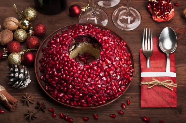 Menu de Natal e Ano Novo: salada 'Garnet Bracelet' (que contém batatas, cebolas fritas, frango frito, beterraba fervida e grãos de romã) em fundo de madeira marrom. Além de talheres, decorações de Natal, especiarias, cones, ouropel etc . — Fotografia de Stock