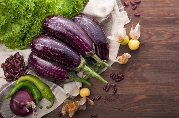 Aubergine mûre juteuse sur une serviette brune sur une surface en bois marron. Près des autres légumes, comme la groseille à maquereau, la laitue, les piments forts, les oignons et les haricots rouges. Végétarien, concept végétalien. Produits agricoles biologiques naturels — Photo