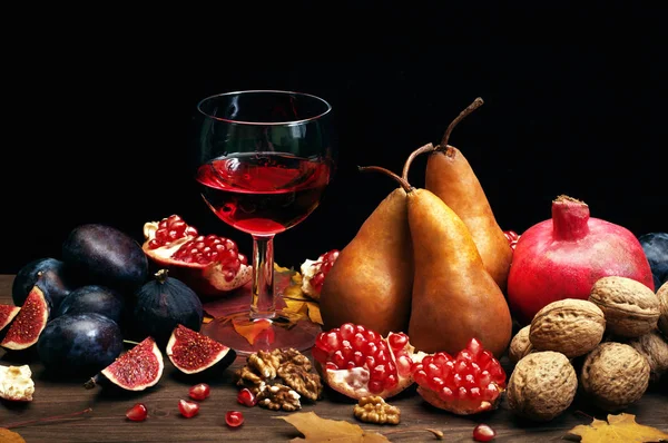 Composizione autunnale con un bicchiere di vino rosso con melograno su fondo scuro. Frutti autunnali come fichi, pere e melograni, e noci. Vegetariano, concetto vegano — Foto Stock