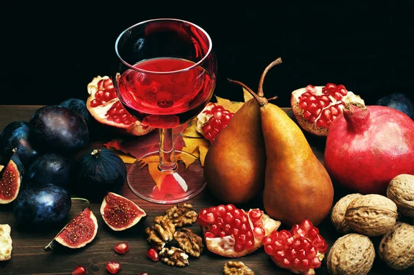 Осенняя композиция с бокалом красного вина с гранатом на темном фоне. Следующие осенние фрукты, такие как инжир, груши и гранаты, и грецкие орехи. Вегетарианская, веганская концепция — стоковое фото