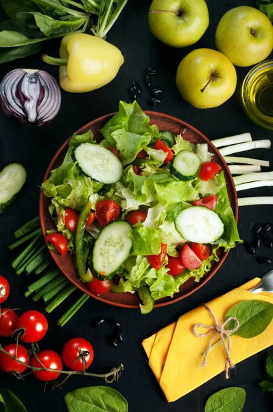 Luminosa y jugosa ensalada vegana de dieta baja en calorías con tomate, pepino y lechuga en una superficie oscura. Cerca de verduras y verduras, como espinacas, manzanas, pimientos, cebollas verdes. Vegetariano, concepto vegano — Foto de Stock