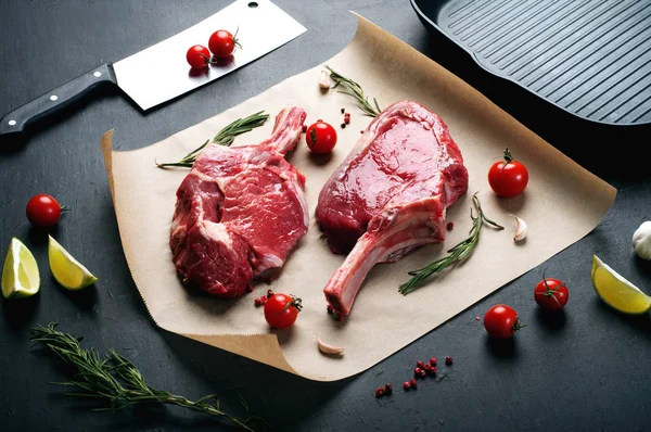 スパイス、調味料、チェリー トマトの横に羊皮紙に生の牛肉ステーキ (肉の塊) 肉。暗い背景 — ストック写真
