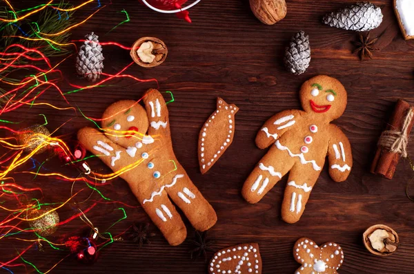 Gingerbread man, Christmas toys and decorations, nuts, cinnamon, anise and other attributes of Christmas on brown wooden background. Photo executed in the technique of mixed light — Stock Photo, Image