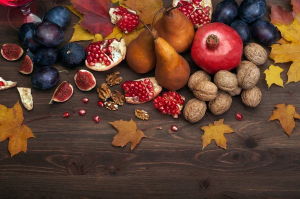 フルーツ、梨、イチジク、プラム、ザクロ、クルミ、茶色の木製の背景に黄色の秋の紅葉などの秋の背景 (壁紙)。ベジタリアン、ビーガンの概念。テキストのためのスペース — ストック写真