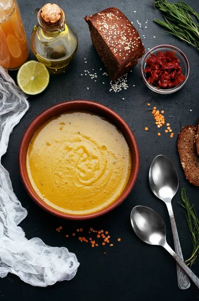 Lentil soup with rosemary, zira, mint and other spices in brown earthenware plate on dark background. Close grain red lentils, spices and seasonings, rye bread, vegetables. Vegetarian, vegan concept — Stock Image Lentil soup with rosemary, zira, mint and other spices in brown earthenware plate on dark background. Close grain red lentils, spices and seasonings, rye bread, vegetables. Vegetarian, vegan concept Royalty Free Stock Photos