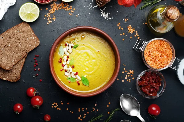 Lentil soup with rosemary, zira, mint and other spices in brown earthenware plate on dark background. Close grain red lentils, spices and seasonings, rye bread, vegetables. Vegetarian, vegan concept — Stock Image Lentil soup with rosemary, zira, mint and other spices in brown earthenware plate on dark background. Close grain red lentils, spices and seasonings, rye bread, vegetables. Vegetarian, vegan concept Royalty Free Stock Photos