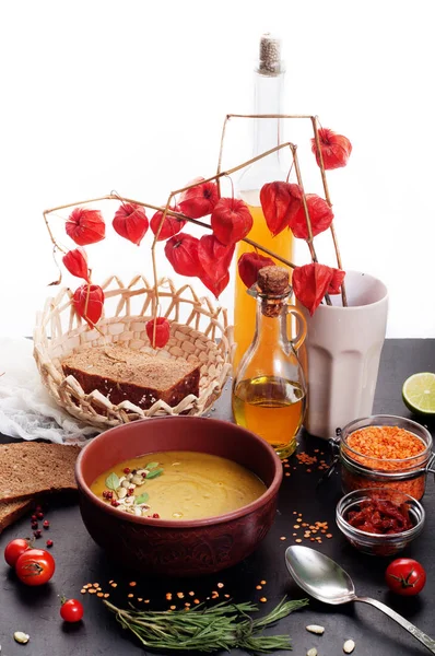 Lentil soup with rosemary, zira, mint and other spices in brown earthenware plate on dark surface, white background. Close grain red lentils, spices and seasonings, rye bread, vegetables. Vegetarian, vegan concept. Place for text — Stock Image Lentil soup with rosemary, zira, mint and other spices in brown earthenware plate on dark surface, white background. Close grain red lentils, spices and seasonings, rye bread, vegetables. Vegetarian, vegan concept. Place for text Stock Picture