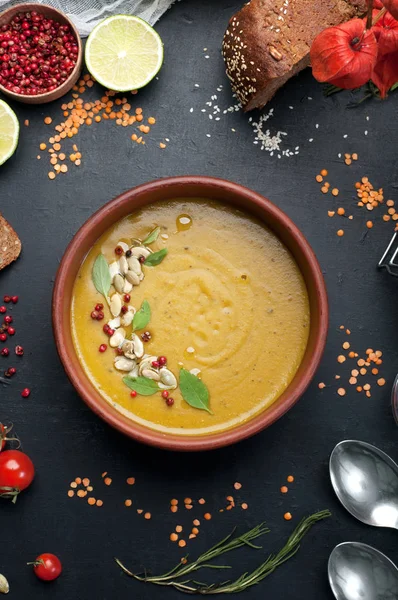 Lentil soup with rosemary, zira, mint and other spices in brown earthenware plate on dark background. Close grain red lentils, spices and seasonings, rye bread, vegetables. Vegetarian, vegan concept — Stock Image Lentil soup with rosemary, zira, mint and other spices in brown earthenware plate on dark background. Close grain red lentils, spices and seasonings, rye bread, vegetables. Vegetarian, vegan concept Stock Photo