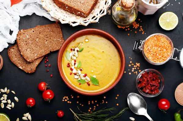 Lentil soup with rosemary, zira, mint and other spices in brown earthenware plate on dark background. Close grain red lentils, spices and seasonings, rye bread, vegetables. Vegetarian, vegan concept — Stock Image Lentil soup with rosemary, zira, mint and other spices in brown earthenware plate on dark background. Close grain red lentils, spices and seasonings, rye bread, vegetables. Vegetarian, vegan concept Stock Picture