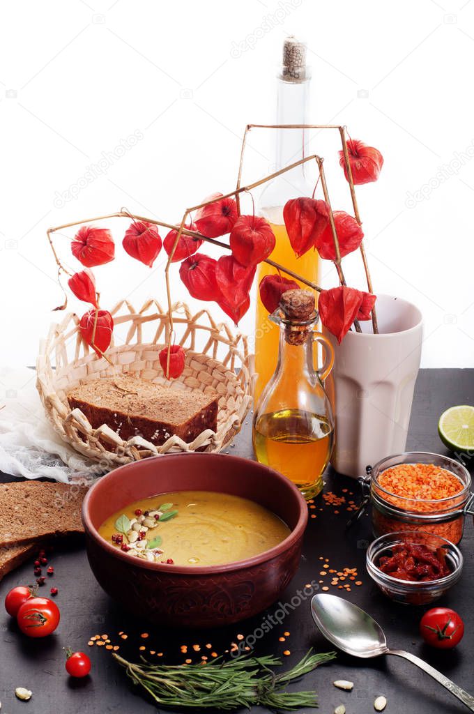 Lentil soup with rosemary, zira, mint and other spices in brown earthenware plate on dark surface, white background. Close grain red lentils, spices and seasonings, rye bread, vegetables. Vegetarian, vegan concept. Place for text