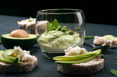 Guacamole - avokado hamuru soğuk meze - karanlık bir arka plan üzerine bir bardak. Avokado ve krem peynir dilimleri ile pirinç ekmek yanında. Meksika mutfağı. Vejetaryen, vegan kavramı 