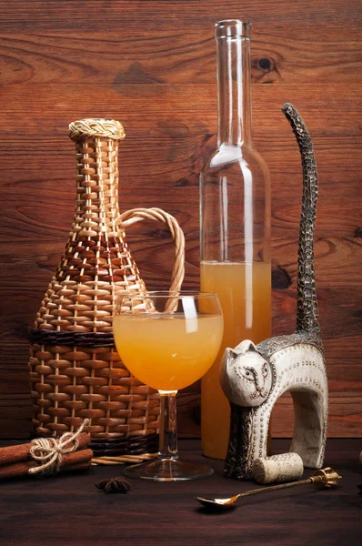 Still-life with cat statuette, homemade cider in bottle and glass on brown wooden background. Low-alcoholic apple drink