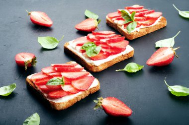 Işık sandviçler tost, az yağlı krem peynir ve çilek dilimleri ile karanlık bir arka plan bahar. Kolay ev yapımı Kahvaltı.