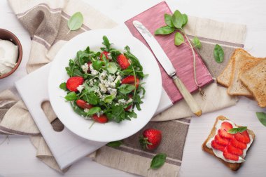 Roka, çilek, mavi peynir ve zeytin yağı beyaz tabakta salatası. Düşük kalorili diyet sağlıklı yemek. Mevsimlik ürünler. Tost, az yağlı yumuşak peynir ve çilek sandviçle kapatın.