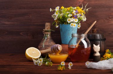 Honey of different colors in different capacities on a brown wooden board. Beside a bouquet of wildflowers. clipart