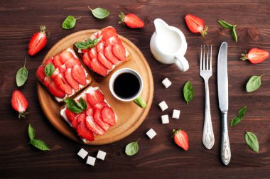 Sandviçler tost, az yağlı krem peynir ve bir yuvarlak Ahşap doğrama tahtası üzerinde çilek ile. Çevre çatal bıçak takımı, kahve ve krem bir sürahi, bardak. Yararlı ve lezzetli mevsimlik kahvaltı kavramı