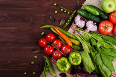 Parlak sulu sebze arka planı (duvar kağıdı). Taze organik ürünler, ıspanak, domates, genç yeşil bezelye, mor fesleğen ve kahverengi ahşap tahta üzerinde biber gibi. Vejetaryen, vegan kavramı