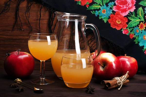 Glass jar with apple cider and glasses of apple cider on a brown wooden background. Near cinnamon, anise stars and red juicy apples. Low-alcohol drink (apple wine), homemade