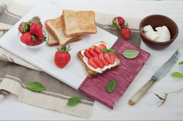 Sandwich with toast, low-fat cream cheese and strawberry on a white cutting board. The concept of useful seasonal breakfast.