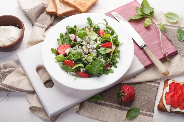 Salat mit Rucola, Erdbeeren, Blauschimmelkäse und Olivenöl auf einem weißen Teller. Kalorienarme Ernährung gesundes Gericht. Saisonprodukte. Sandwich mit Toast, fettarmem Weichkäse und Erdbeeren schließen. — Stockfoto