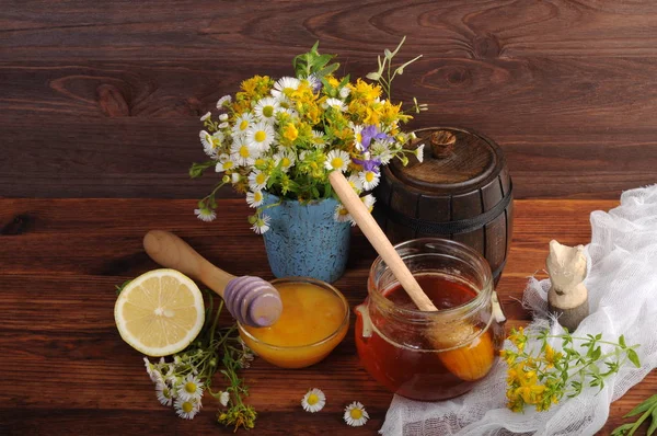 Miel de diferentes colores en diferentes capacidades sobre una tabla de madera marrón. Junto a un ramo de flores silvestres . — Foto de Stock