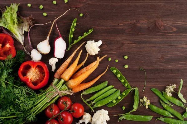 Vegetabiliska bakgrund (skrivbordsunderlägg) med körsbärstomater, röd paprika, unga gröna ärtor och rädisor på brun trä bakgrund. Vegetarisk, vegan koncept. Utrymme för text — Stockfoto