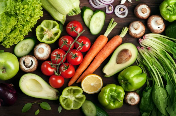 Pflanzlichen Hintergrund (Tapete). Grüner Spinat, Kirschtomaten, Karotten, Paprika, Avocado, Pilze und Zitrone auf einer braunen Holzoberfläche. vegetarisches, veganes Konzept — Stockfoto