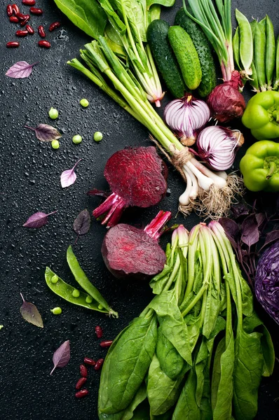 Legumes orgânicos coloridos suculentos em um fundo escuro com gotas de água. Pimentos verdes, alface, manjericão roxo, ervilhas verdes jovens, pepino e espinafre. Vegetariano, conceito vegan — Fotografia de Stock