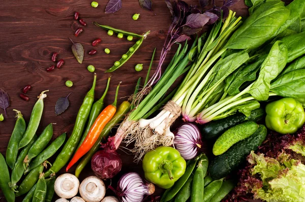 Vegetable background (wallpaper). Bright juicy spinach, purple onion, paprika, colorful hot peppers, purple basil, young green peas and mushrooms on a brown wooden surface. Space for text. Vegetarian, vegan concept — Stock Photo, Image