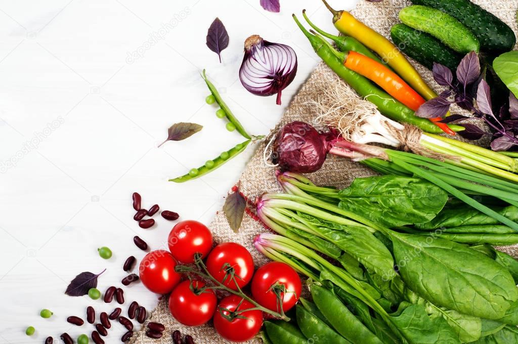 Bright juicy vegetable background (wallpaper). Fresh organic produce, such as spinach, cherry tomatoes, young green peas, purple basil and pepper on white wooden board. Vegetarian, vegan concept