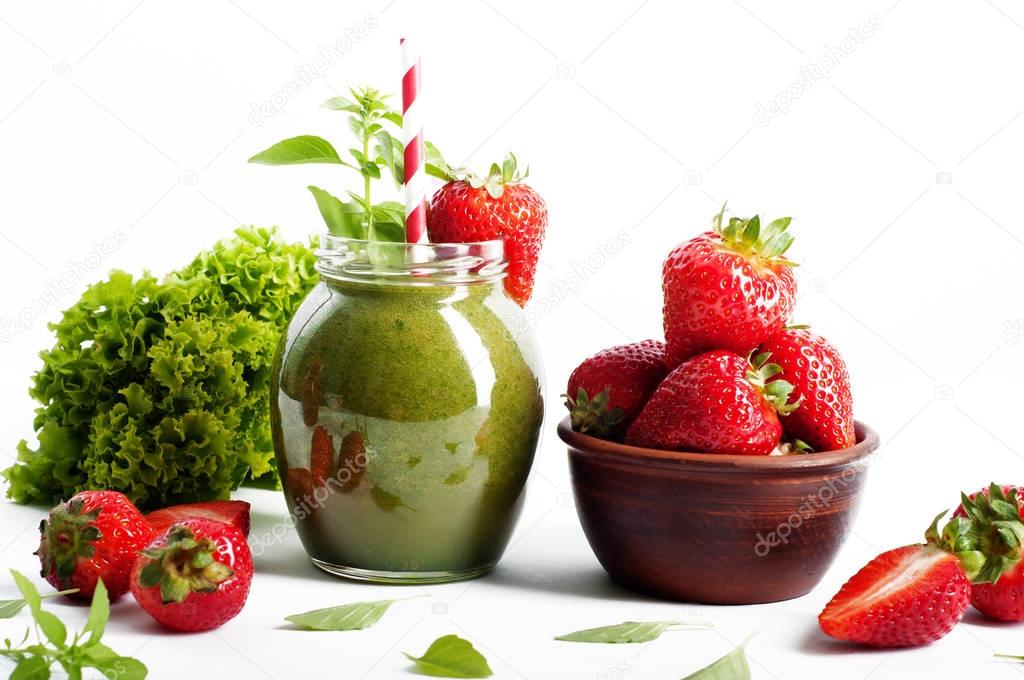 Green smoothie of apples, avocados and spinach in a glass jar on a white background. Near strawberries, basil leaves and lettuce leaves on the background. Vegetarian, vegan concept. Diet drink for detoxification