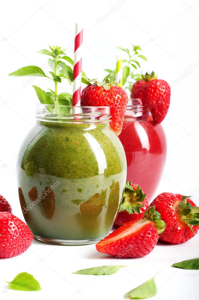 Green smoothie of apples, avocados and spinach in a glass jar on a white background. In the background, strawberry (berry) smoothies. Near strawberries and basil leaves. Vegetarian, vegan concept. Diet drink for detoxification