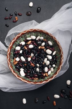 Farklı renklerde karanlık bir arka plan üzerinde vintage bir seramik tabak, fasulye taneleri. Vejetaryen, vegan kavramı
