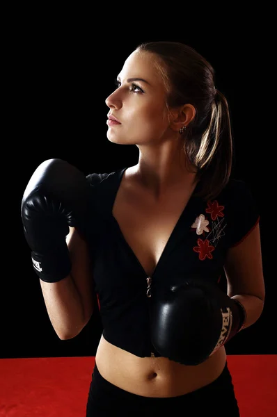 Mulher bonita e magra em top preto na mão usando luvas de boxe em pé na mesa do lutador no fundo preto. O conceito de "fortalecer o corpo e o espírito através do boxe". Retrato da cintura — Fotografia de Stock