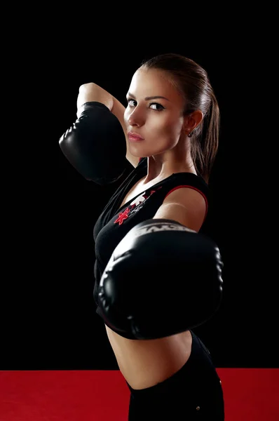 Beautiful slim woman in black top on hand wearing boxing gloves standing in the fighter\'s desk on black background. The concept of \'strengthening the body and spirit by boxing\'. Portrait of the waist