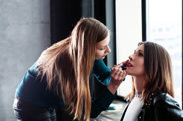 Processen att make-up innan du tar bilden. Flickan - makeup-artist som målar en tjej modell med hjälp av mörkt rött läppstift. Fönstret i bakgrunden. — Stockfoto
