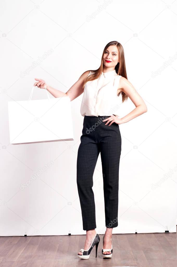 Beautiful young woman (girl) with long light brown hair in a white blouse standing straight and holding a white packages. shopping concept. White background. Portrait in full growth