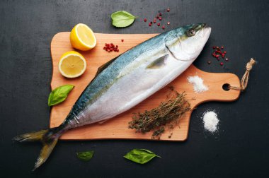 Kavurma tarafından hazırlanan ham ton balığı (bütün balık) mı yalan ahşap kesme tahtası üzerinde limon, otlar ve baharatlar kapatın. Evde yemek tarifleri beslenme (konsept).
