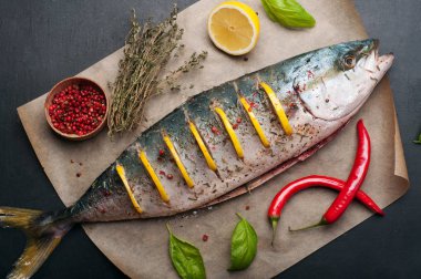 Ham ton balığı (bütün balık) kavurma tarafından hazırlanan limon dilimleri ile yalanlar üzerine bir parşömen, yakın sebzeler, otlar ve baharatlar var. Evde yemek tarifleri beslenme (konsept).