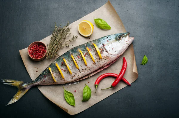 Ham ton balığı (bütün balık) kavurma tarafından hazırlanan limon dilimleri ile yalanlar üzerine bir parşömen, yakın sebzeler, otlar ve baharatlar var. Evde yemek tarifleri beslenme (konsept).