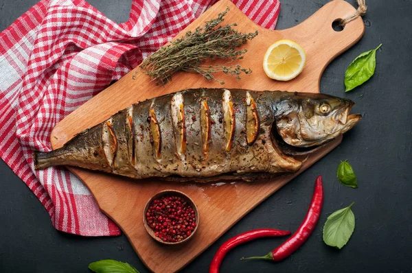 Atún (pescado), al horno con hierbas, especias y rodajas de limón, acostado en una tabla de cortar. Cerca de tomillo, hojas de albahaca, pimienta rosa y pimienta picante. Fondo oscuro. El plato terminado. Cocina mediterránea — Foto de Stock