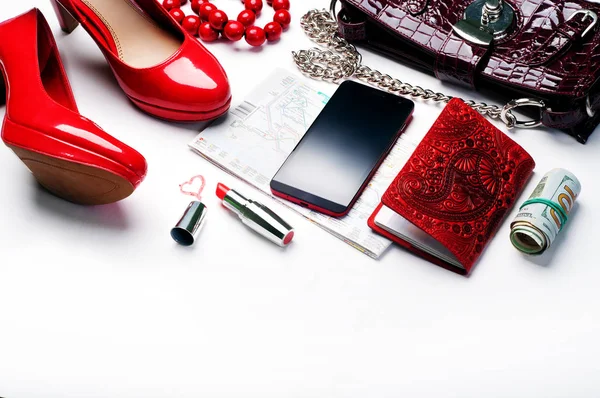 Concept let\'s travel! Red lacquered high heel shoes, passport in red cover, telephone, map of Barcelona, lipstick and a bunch of money on a white background. All you need to travel for a stylish young woman.