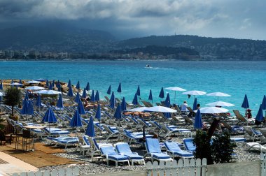 Mavi ve beyaz şemsiye ve şezlong ile ıssız sahilde Cte d'Azur, Cannes, Fransa. Bulutlu. Arka planda dağlar.