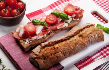 Bir sandviç kepekli ekmek, sarsıntılı, domates ve fesleğen bir kesme tahtası üzerinde bırakır. Lezzetli ve sağlıklı ev yapımı çanak